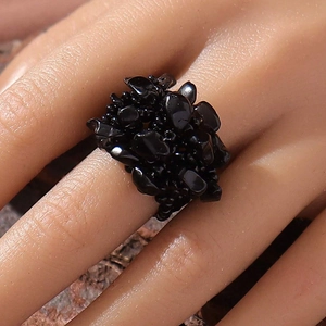 Close-up of a natural black crushed stone cluster ring on a model hand with stone background