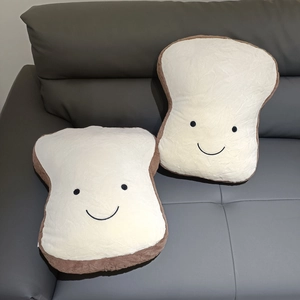 Detail of two plush toast pillows with smiling faces on a grey leather sofa