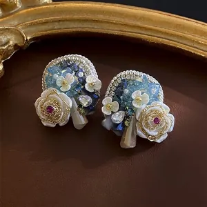 Vintage floral stud earrings with white roses and blue crystal accents on leather background