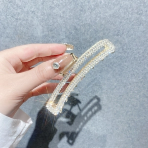 Gros plan d'une pince à cheveux rectangulaire dorée ornée de strass brillants tenue à la main