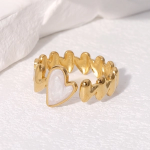 Macro view of adjustable gold ring with white pearl heart charm on a textured background