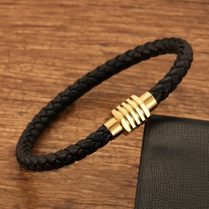 Braided black leather bracelet with golden stainless steel clasp on a wooden desk