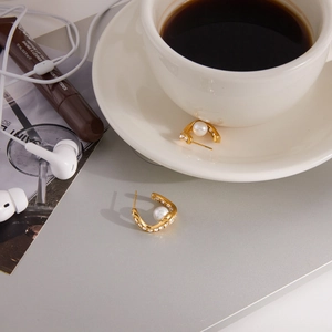 Detailed view of U-shaped gold earrings with white pearls and diamonds on a desktop