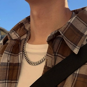 Close-up of a silver cuban link chain worn by a model against a blue sky background