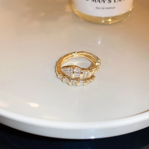 Macro shot of gold snake-shaped ring with square-cut zirconia on white ceramic