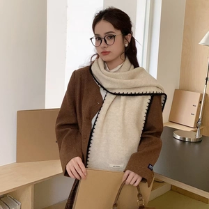 Winter knitted cream scarf with black stitched edges worn with a brown wool coat