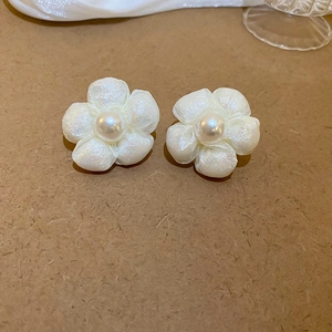 Close-up of white fabric flower earring with a pearl center on brown paper background