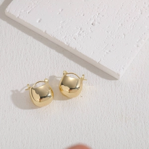 Detailed view of polished gold bean-shaped earrings on textured white stone surface