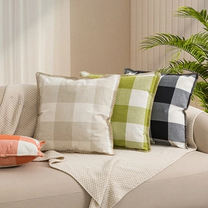 Close-up of four plaid plush pillow covers in beige, green, black and orange on a sofa