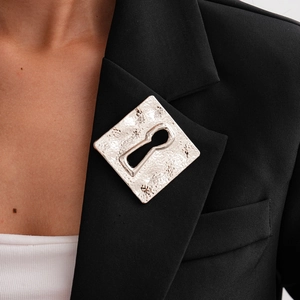 Close-up of a silver hammered square brooch with keyhole detail on a black blazer lapel