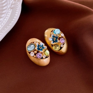 Macro detail of vintage gold enamel floral earrings with colorful crystals on velvet