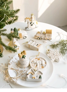 Flat lay of white and gold Christmas ornaments including mini car, house, and reindeer