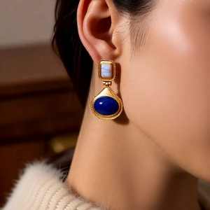 Detail of vintage gold earrings with light blue square and oval dark blue stones on a model