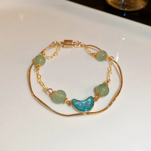Detail view of double-layer gold chain bracelet with green beads and blue moon pendant