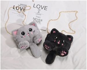 Flat lay of grey and black plush cat crossbody bags with gold metal chains on white fabric