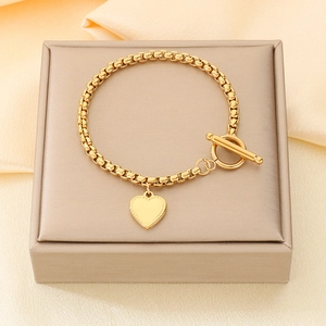 Dettaglio del bracciale con ciondolo a cuore dorato e chiusura OT su portagioie in seta