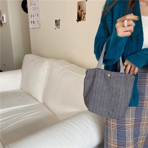 Detailed side view of a black and white herringbone wool tote bag with a gold button closure