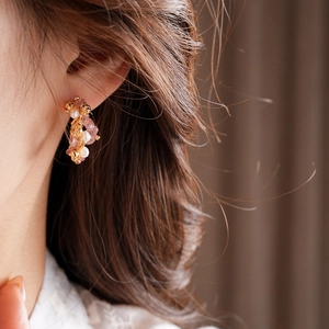 Detail of C-shaped gold earrings with strawberry quartz, pearls, and rose design on ear