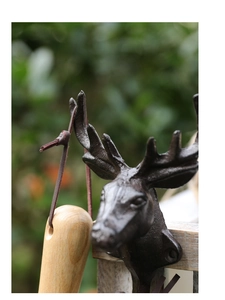 Close-up of vintage cast iron deer head wall hook mounted on a wooden garden fence