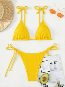 Flat lay of bright yellow ribbed bikini with sunglasses and straw hat on white backdrop