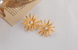 Detail of golden sunburst earrings featuring a central white pearl and a textured background