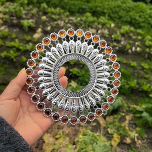 Detail of silver sunburst wall decor with amber stones held by hand in a garden