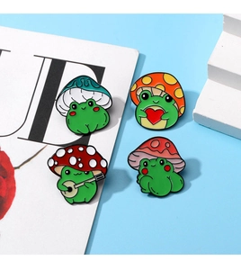 Macro detail of four cute enamel frog pins wearing mushroom hats on a blue background