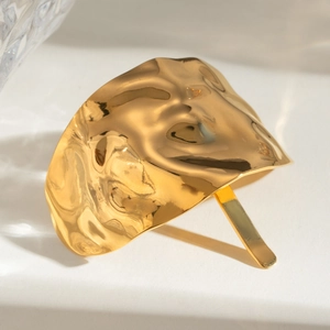 Macro shot of gold-plated hair pin with hammered texture on white marble surface
