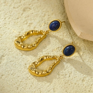 Macro detail of gold textured earrings with blue turquoise stones on stone background