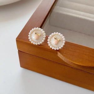 Detail view of round floral earrings with white enamel, pearls, and golden bow decoration