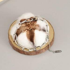 Detailed view of silver stainless steel chain bracelet with K18 tag on wooden base