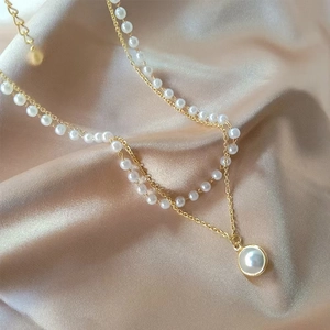 Double-layer gold necklace with pearls and round pendant on champagne silk fabric
