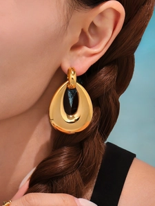 Close-up of polished gold-plated hollow teardrop earrings on a model with blue background