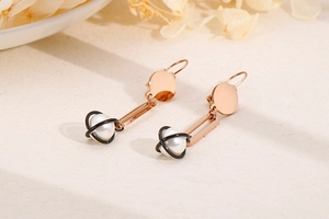 Detail of rose gold long pearl earrings with black metal frames on a neutral textured background