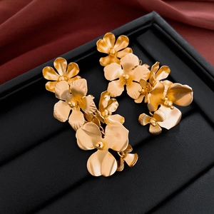 Macro shot of matte gold layered flower earrings on black leather with red silk