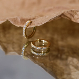 Artistic macro shot of golden crystal square hoop earrings on a reflective brown surface