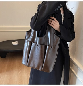 Detail of dark brown leather tote bag with three utility front pockets and metal rivets
