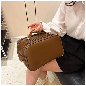 Brown PU leather toiletry bag with handle and double zipper shown in a lifestyle setting