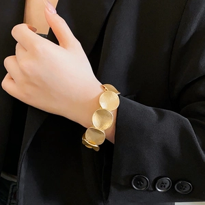 Close-up of a gold hammered circular geometric bracelet worn over a black blazer cuff
