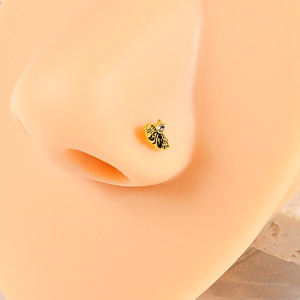 Macro detail of a golden bee nose stud with a clear crystal on a realistic nose model