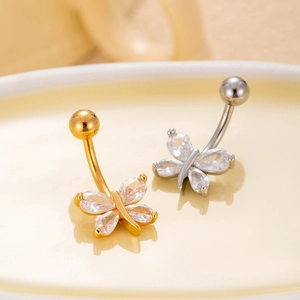 Macro shot of gold and silver butterfly navel rings with cubic zirconia on a cream plate