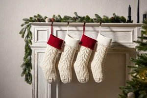 Close-up of knit Christmas stockings with heart tassels hanging on a festive white fireplace