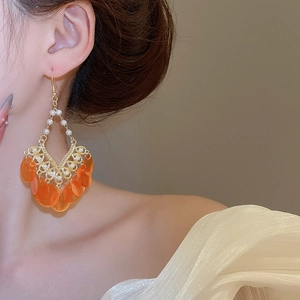 Detailed view of bohemian tassel earrings with orange shell discs and white pearls on a model