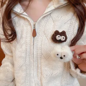 Cute plush cartoon monster brooches in brown and white on a knitted cardigan