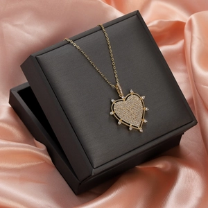 Macro detail of gold-plated heart pendant with zircons on elegant pink silk fabric