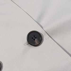 Close-up of grey coat fabric featuring a black four-hole button and detailed stitching