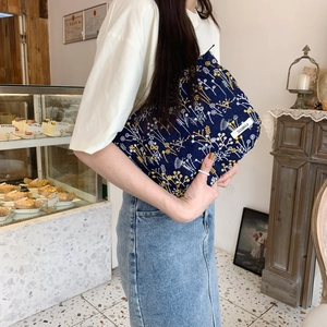 Navy blue pouch with yellow flower embroidery held by a model in a cafe setting
