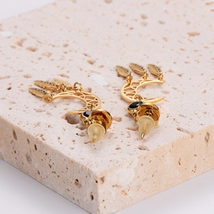 Elegant gold crescent moon earrings with leaf tassels and black gemstones on a stone base