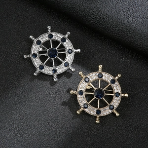 Sailing helm brooch with silver and gold finishes and navy blue gemstones on black background