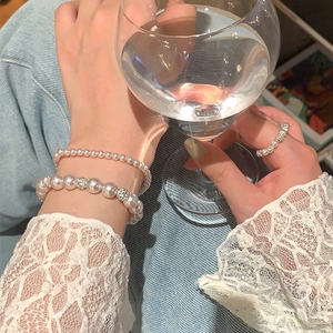 Détail de bracelets en perles superposés avec boule de diamant et bague en perle assortie